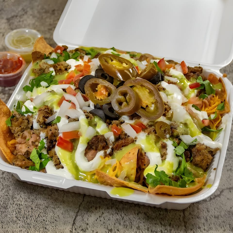 Juanitas III nachos in a to-go container, topped with meat, cheese, jalapenos, and sauces.