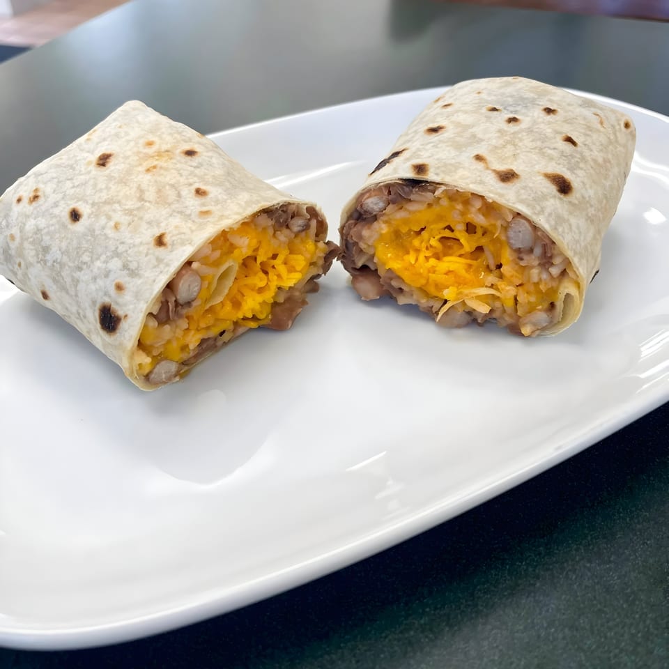 A Juanitas III burrito, cut in half, revealing melted cheese, rice, and beans on a white plate.