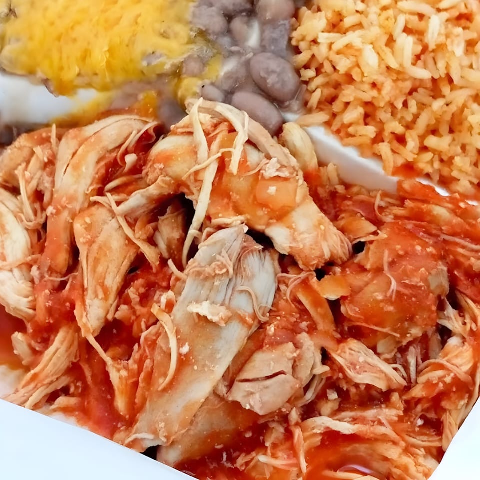 Shredded chicken in red sauce, with rice, beans, and melted cheese on a white plate.