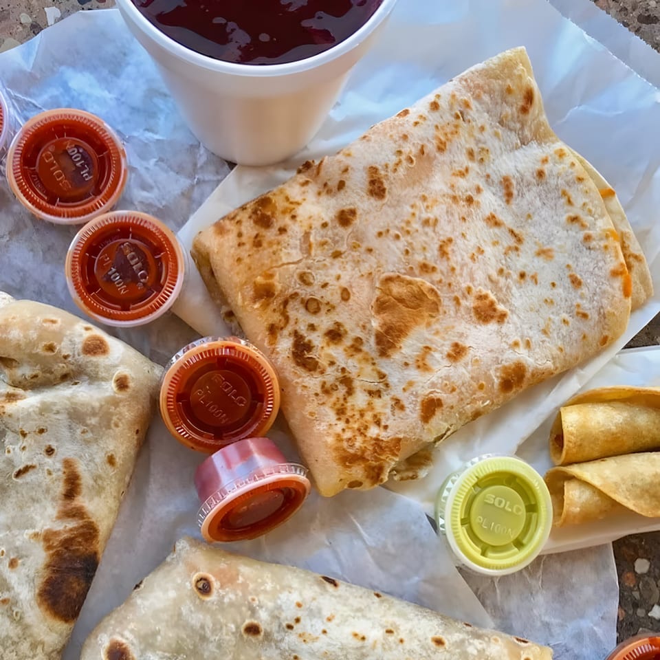 Burritos, taquitos, and various sauces from Juanitas III Rancho Cucamonga, on white paper.
