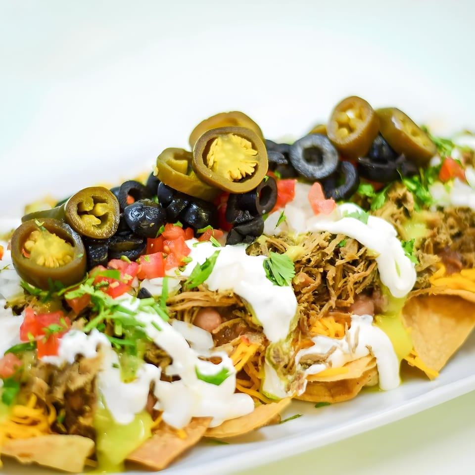Close-up of Juanitas III nachos with shredded meat, jalapeños, olives, tomatoes, and sour cream.
