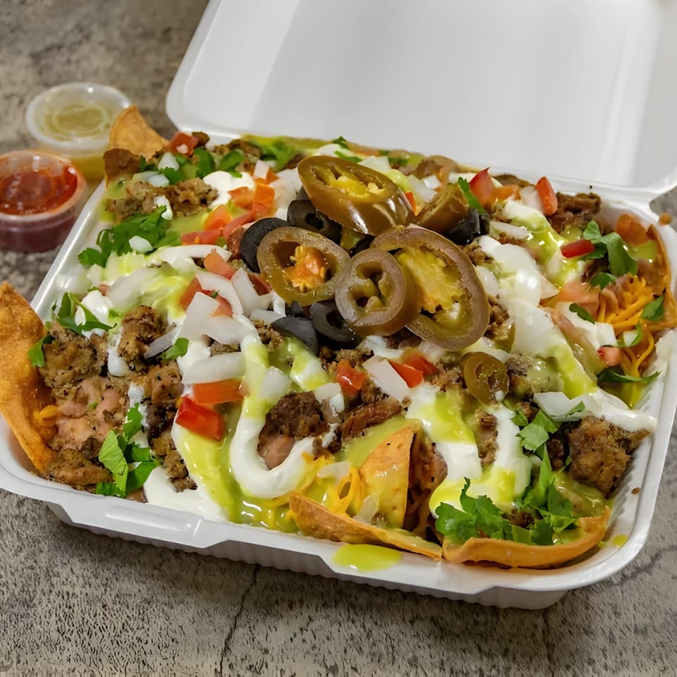 Juanitas III nachos with meat, cheese, jalapeños, olives, and sauces in a takeout container.
