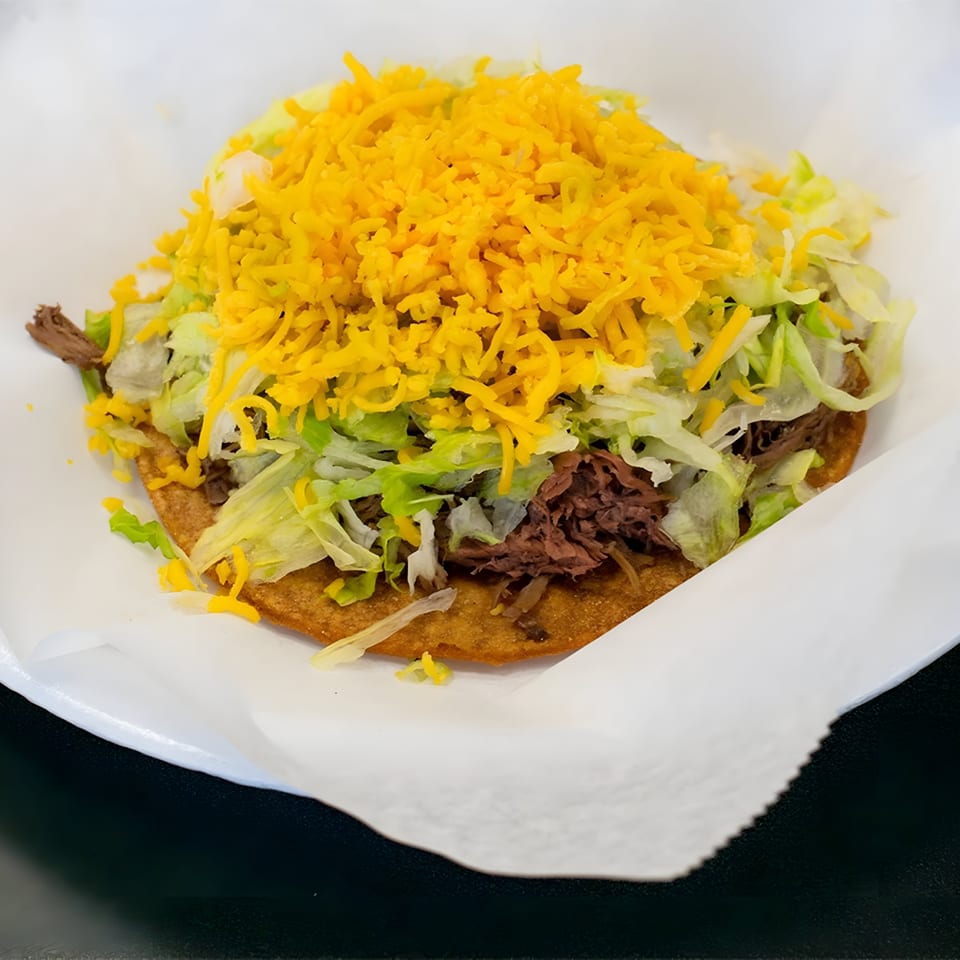 A Juanitas III tostada with shredded beef, lettuce, and a generous topping of shredded cheddar cheese.